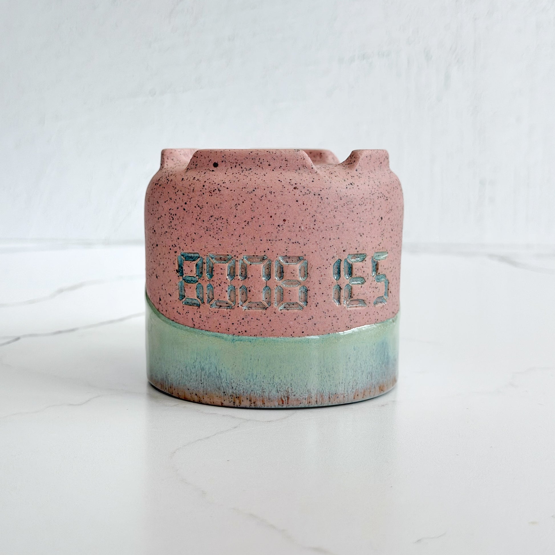 A handmade pink speckled clay ceramic cup by Kathleen Kalish Ceramics with mint green glaze. Flipped upside down. Stamped with BOOBIES. For the Boobless Project helping breast cancer.