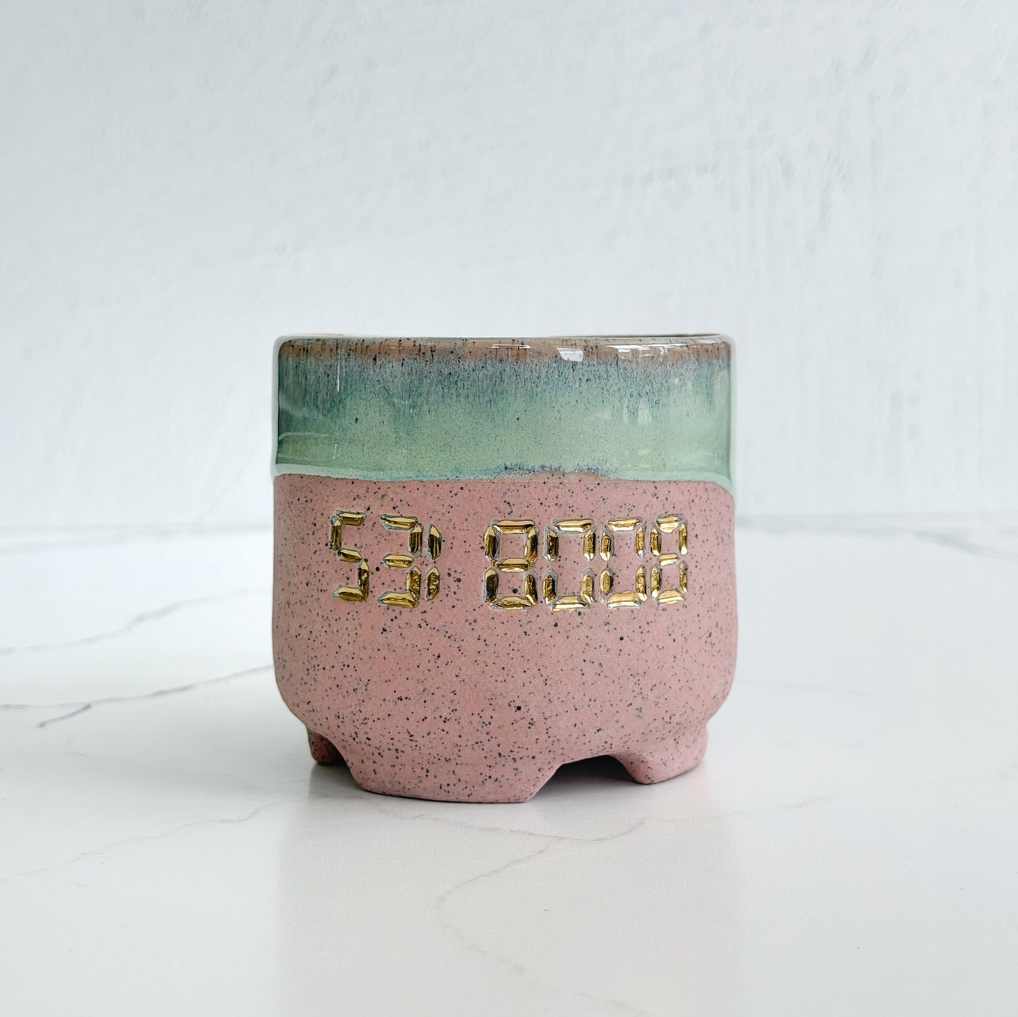 A handmade pink speckled clay ceramic cup by Kathleen Kalish Ceramics with green glaze. Stamped with 5318008 and decorated with gold luster. For the Boobless Project helping breast cancer.