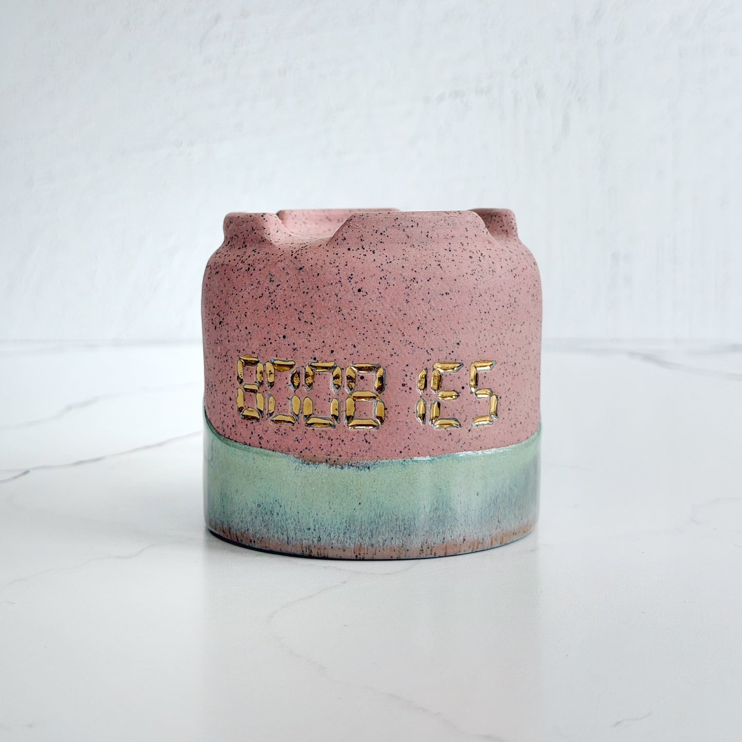 A handmade pink speckled clay ceramic cup by Kathleen Kalish Ceramics with green glaze. Stamped with BOOBIES and decorated with gold luster. For the Boobless Project helping breast cancer.