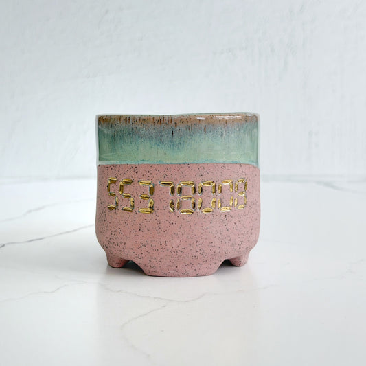 A handmade pink speckled clay ceramic cup by Kathleen Kalish Ceramics with green glaze. Stamped with 55378008 and decorated with gold luster. For the Boobless Project helping breast cancer.