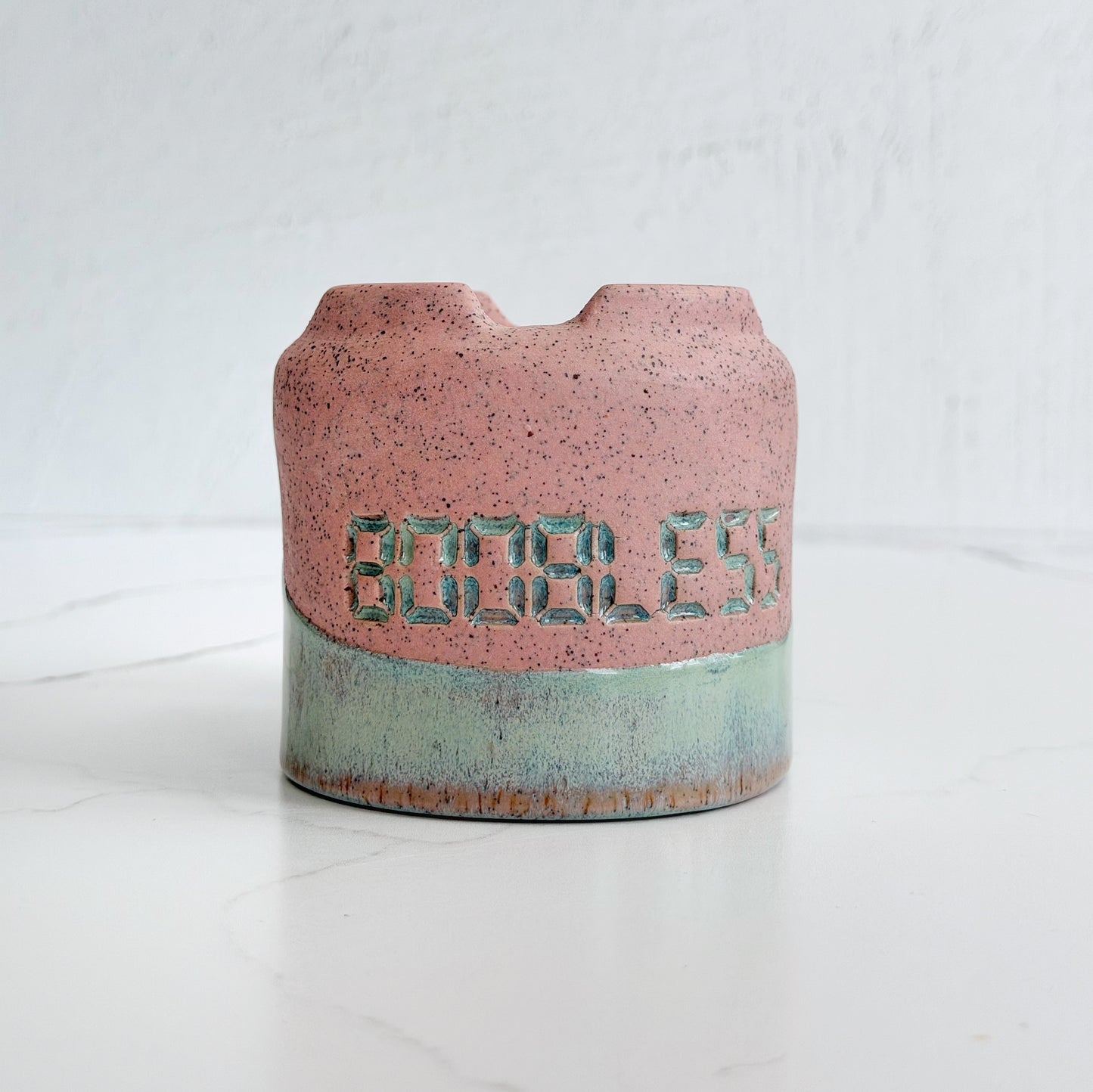 A handmade pink speckled clay ceramic cup by Kathleen Kalish Ceramics with mint green glaze. Flipped upside down. Stamped with BOOBLESS. For the Boobless Project helping breast cancer.