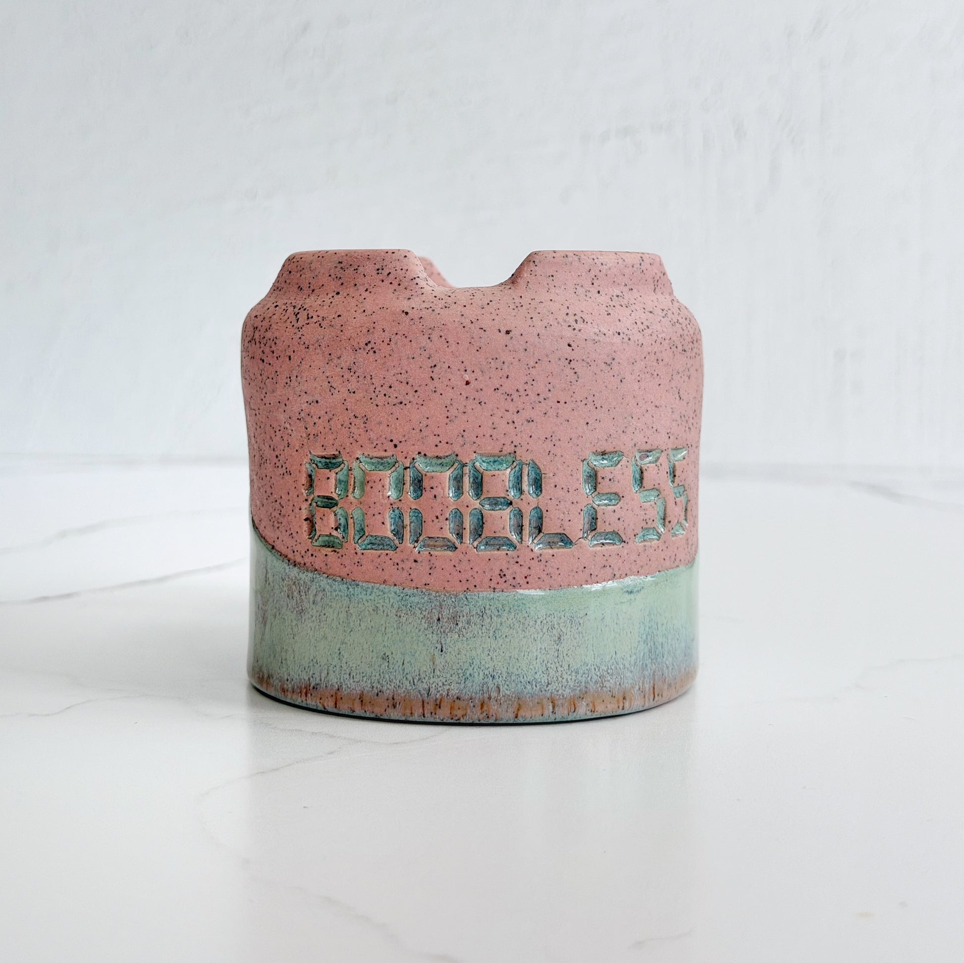 A handmade pink speckled clay ceramic cup by Kathleen Kalish Ceramics with mint green glaze. Flipped upside down. Stamped with BOOBLESS. For the Boobless Project helping breast cancer.
