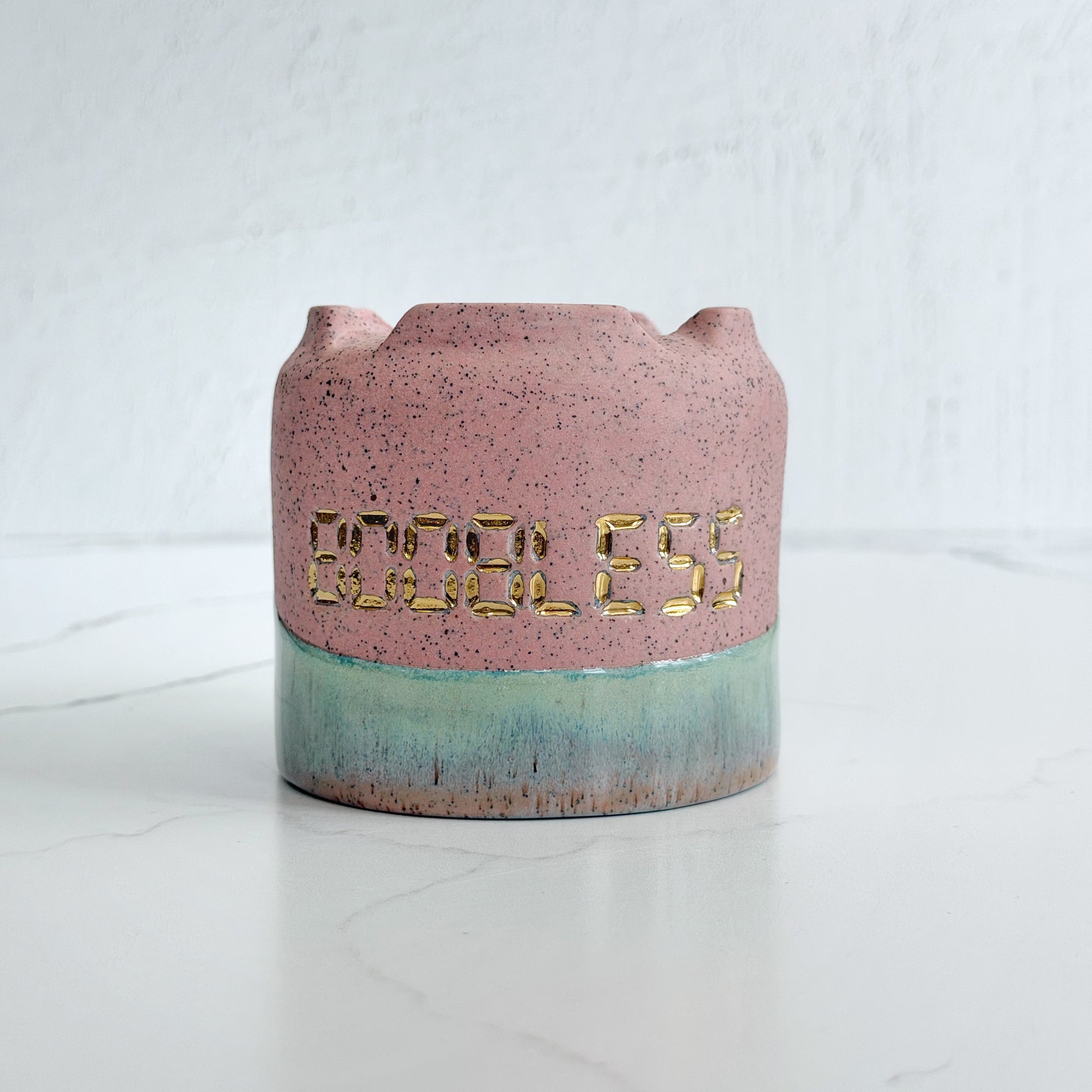 A handmade pink speckled clay ceramic cup by Kathleen Kalish Ceramics with green glaze. Stamped with BOOBLESS and decorated with gold luster. For the Boobless Project helping breast cancer.