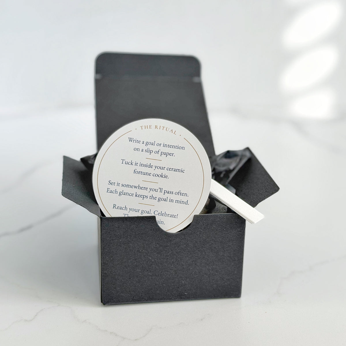 A black gift box with a circular white insert card reading 'The Ritual' and instructions for the Make Your Own Fortune Set.