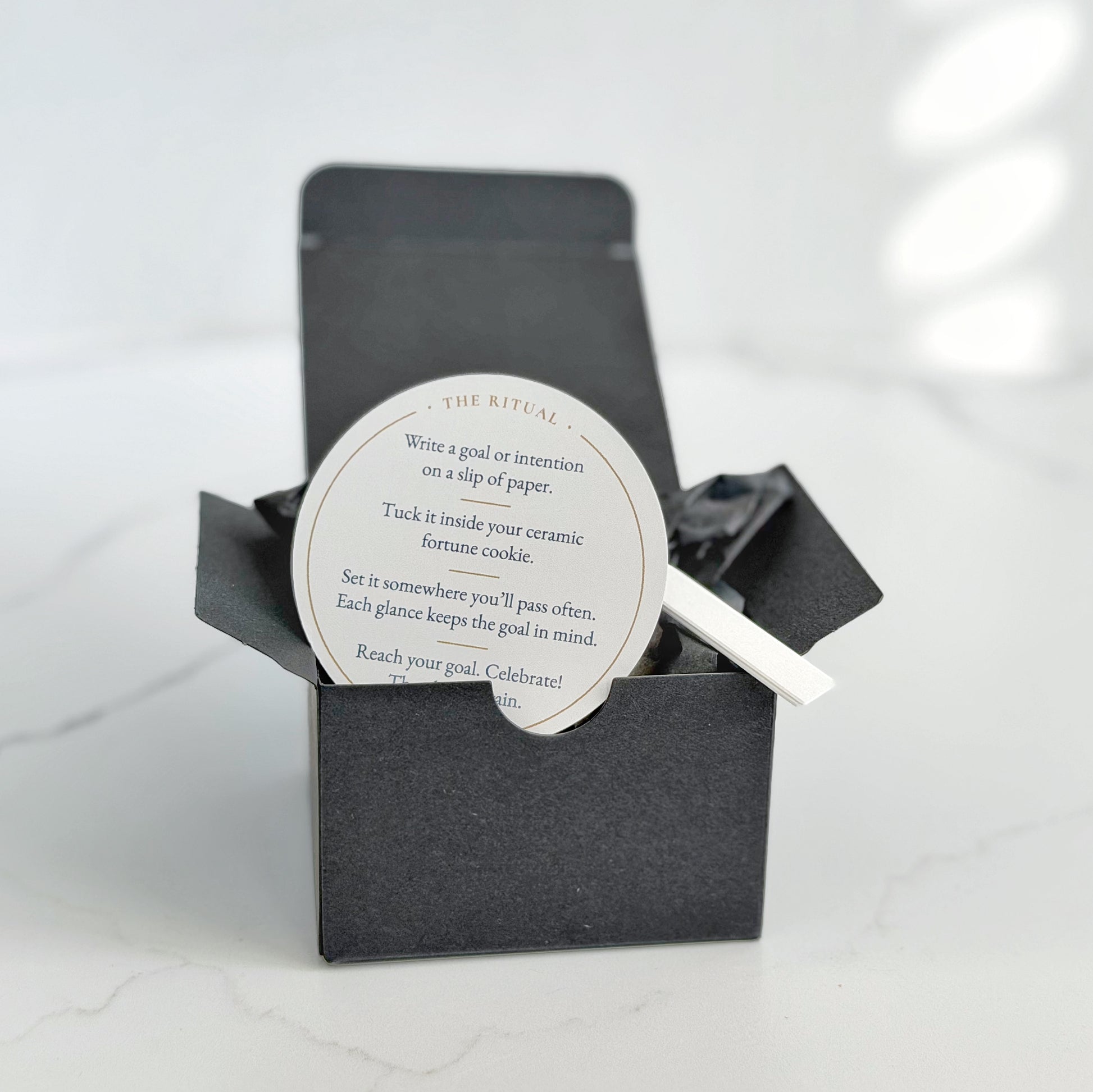 A black gift box with a circular white insert card reading 'The Ritual' and instructions for the Make Your Own Fortune Set.