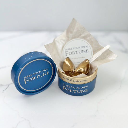A blue and gold round gift box with a antique gold fortune cookie inside. Text on box reads Make Your Own Fortune.