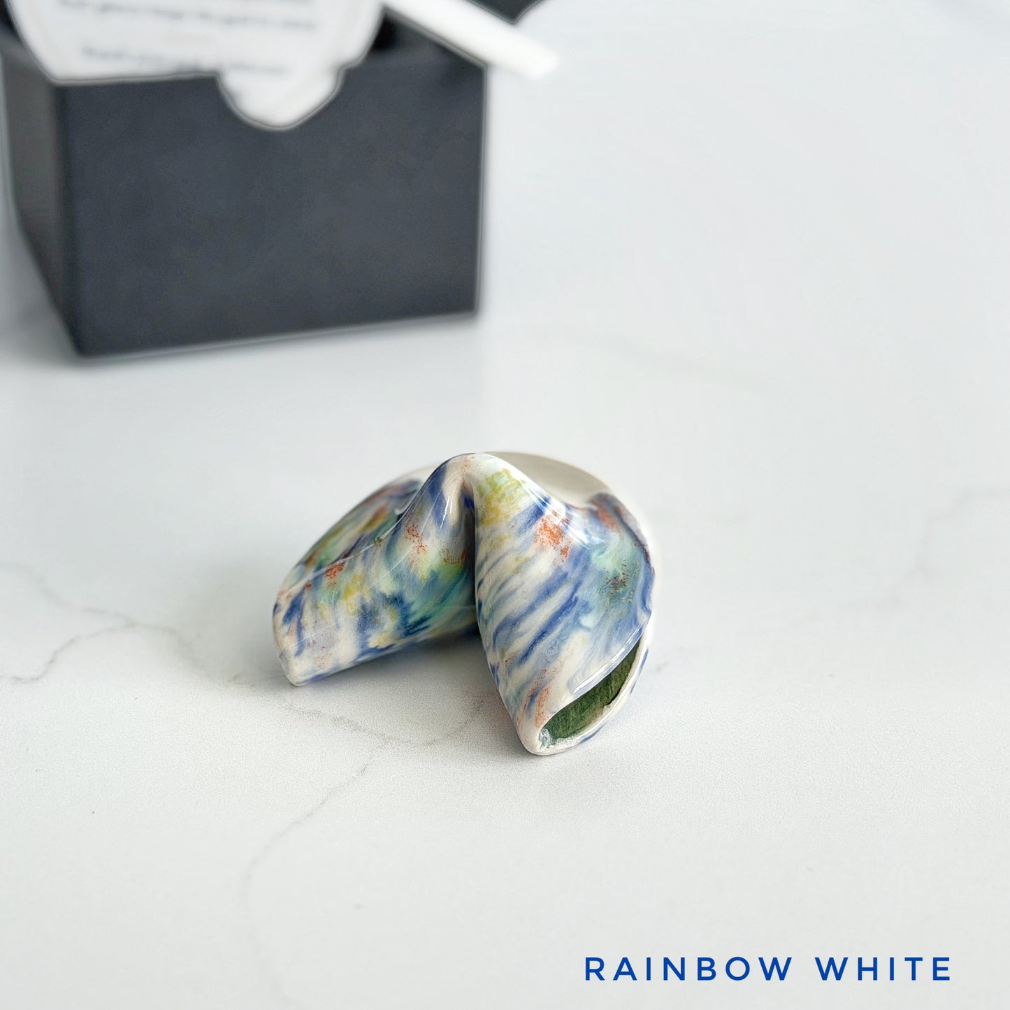 White and multi colored glaze streaks on a ceramic fortune cookie, handmade and glazed by hand in Wilmington, NC by Kathleen Kalish Ceramics.